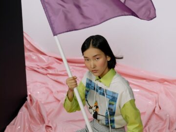 A young woman sits indoors holding a flag with 'Kindness' on it, embodying peaceful protest.
