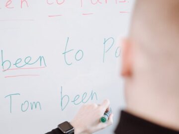 A person writing grammar instructions on a whiteboard with a marker.