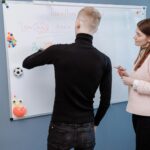 A student and teacher engage in an English lesson on a whiteboard. Indoor educational setting.