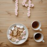 Top view of heart-shaped cookies with tea and marshmallows forming the number 14 on a wooden surface.