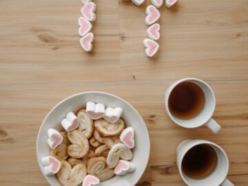 Top view of heart-shaped cookies with tea and marshmallows forming the number 14 on a wooden surface.