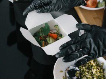 Gloved hands preparing fresh salad takeout in eco-friendly containers for delivery.