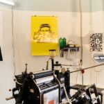 A detailed view of a professional printing press setup in a studio, highlighting equipment and posters.