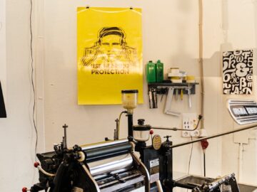 A detailed view of a professional printing press setup in a studio, highlighting equipment and posters.
