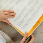 Close-up of a woman's hands holding an open book on a sofa, focusing on text details.
