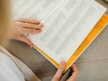 Close-up of a woman's hands holding an open book on a sofa, focusing on text details.