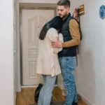 An emotional couple embraces in a hallway, conveying sadness and comfort at home.