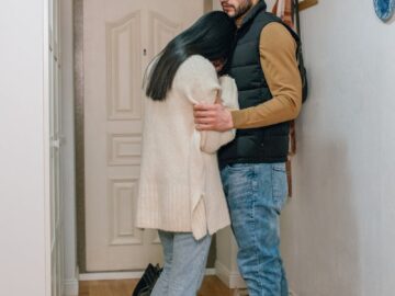 An emotional couple embraces in a hallway, conveying sadness and comfort at home.