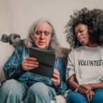 Young volunteer helps senior man with technology, fostering connection indoors.