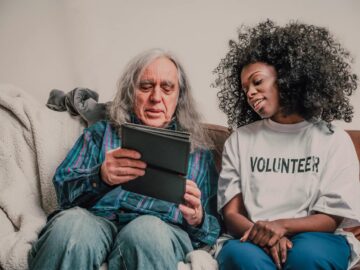 Young volunteer helps senior man with technology, fostering connection indoors.