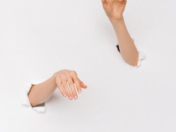 An artistic shot of two hands emerging from a white wall, symbolizing creativity and expression.
