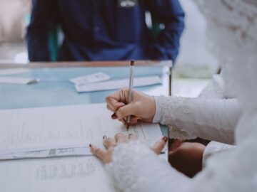 Bride signing marriage documents with witnesses during the wedding ceremony indoors.