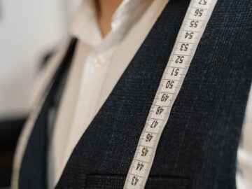 Close-up of a tailor in a suit with a measuring tape across his shoulders.