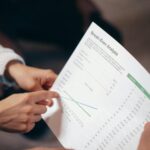 Close-up of hands discussing a break-even analysis document in a business meeting.
