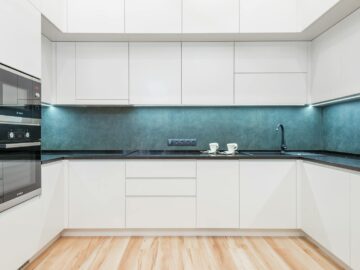 Interior of white modern kitchen with minimalist design of white cabinets blue backsplash and black built in appliances