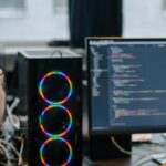 Two programmers discussing code on a monitor in a tech workspace, focusing on collaboration.