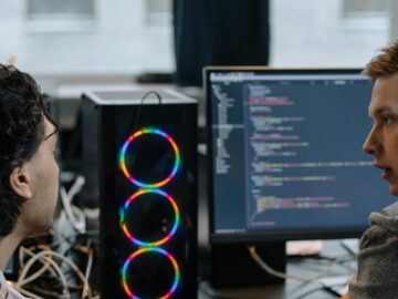 Two programmers discussing code on a monitor in a tech workspace, focusing on collaboration.