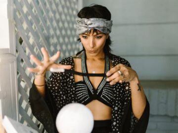 Mystical woman in patterned attire performing a ritual with crystal ball indoors.