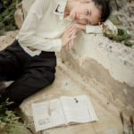 A serene moment captured of a woman leaning on a stone surface beside an open book outdoors.