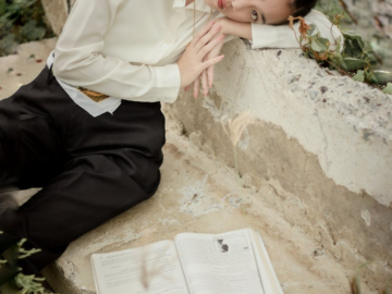 A serene moment captured of a woman leaning on a stone surface beside an open book outdoors.