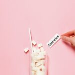 Glass of sugar cubes with diabetes label on pink background.