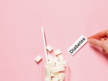 Glass of sugar cubes with diabetes label on pink background.