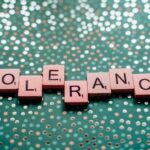 Close-up of scrabble tiles spelling 'tolerance' on a turquoise background.