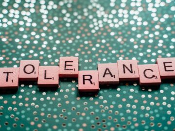 Close-up of scrabble tiles spelling 'tolerance' on a turquoise background.