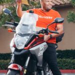 Smiling delivery man on a motorcycle holding an envelope, ready for delivery.