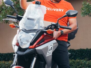 Smiling delivery man on a motorcycle holding an envelope, ready for delivery.