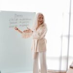 Elderly female instructor teaches English grammar in a bright classroom setting.