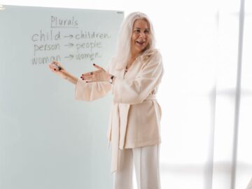 Elderly female instructor teaches English grammar in a bright classroom setting.