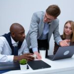 Three professionals engage in a lively business discussion at a modern office desk, focusing on teamwork.