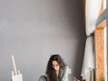 A young woman in casual attire painting on the floor of a modern studio with natural light.