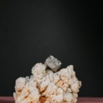 A striking still life of a pyrite crystal on calcite against a dark background.
