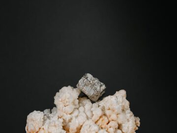 A striking still life of a pyrite crystal on calcite against a dark background.