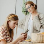A mother discusses with her daughter engrossed in her phone during breakfast indoors.
