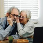 Senior couple affectionately using a laptop together at a table in their cozy home.