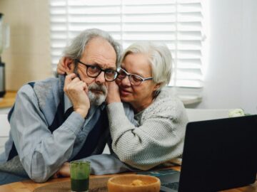 Senior couple affectionately using a laptop together at a table in their cozy home.
