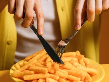 A young man enjoying a plate of crispy snacks with a knife and fork against a yellow background.