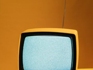 Retro yellow television on orange backdrop with static screen, perfect for vintage themes.