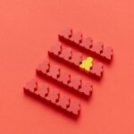 A group of red meeples with one yellow meeple standing out on a red background, symbolizing individuality.