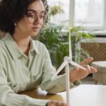 Focused young woman studying a wind turbine model indoors, highlighting renewable energy and education.