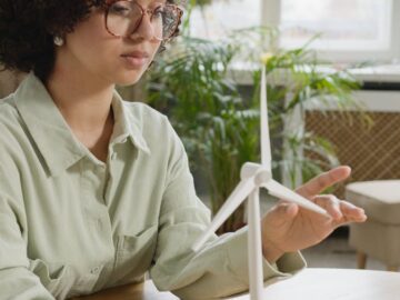 Focused young woman studying a wind turbine model indoors, highlighting renewable energy and education.