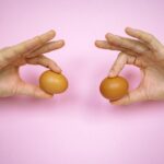 Two hands holding brown eggs against a pastel pink background, close-up.