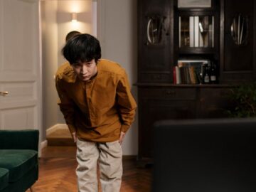 A young Asian man bows in front of a laptop while at home, symbolizing a greeting or training session.