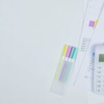 Minimalist office desk with a calculator, budget planning documents, and colorful pens.