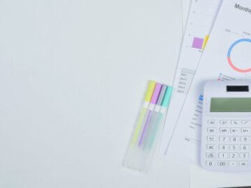 Minimalist office desk with a calculator, budget planning documents, and colorful pens.