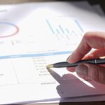 Hand holding pen, analyzing budget with charts and graph paper.