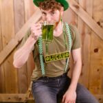 Caucasian man in green attire enjoying St. Patrick's Day with a mug of green beer and festive costume.
